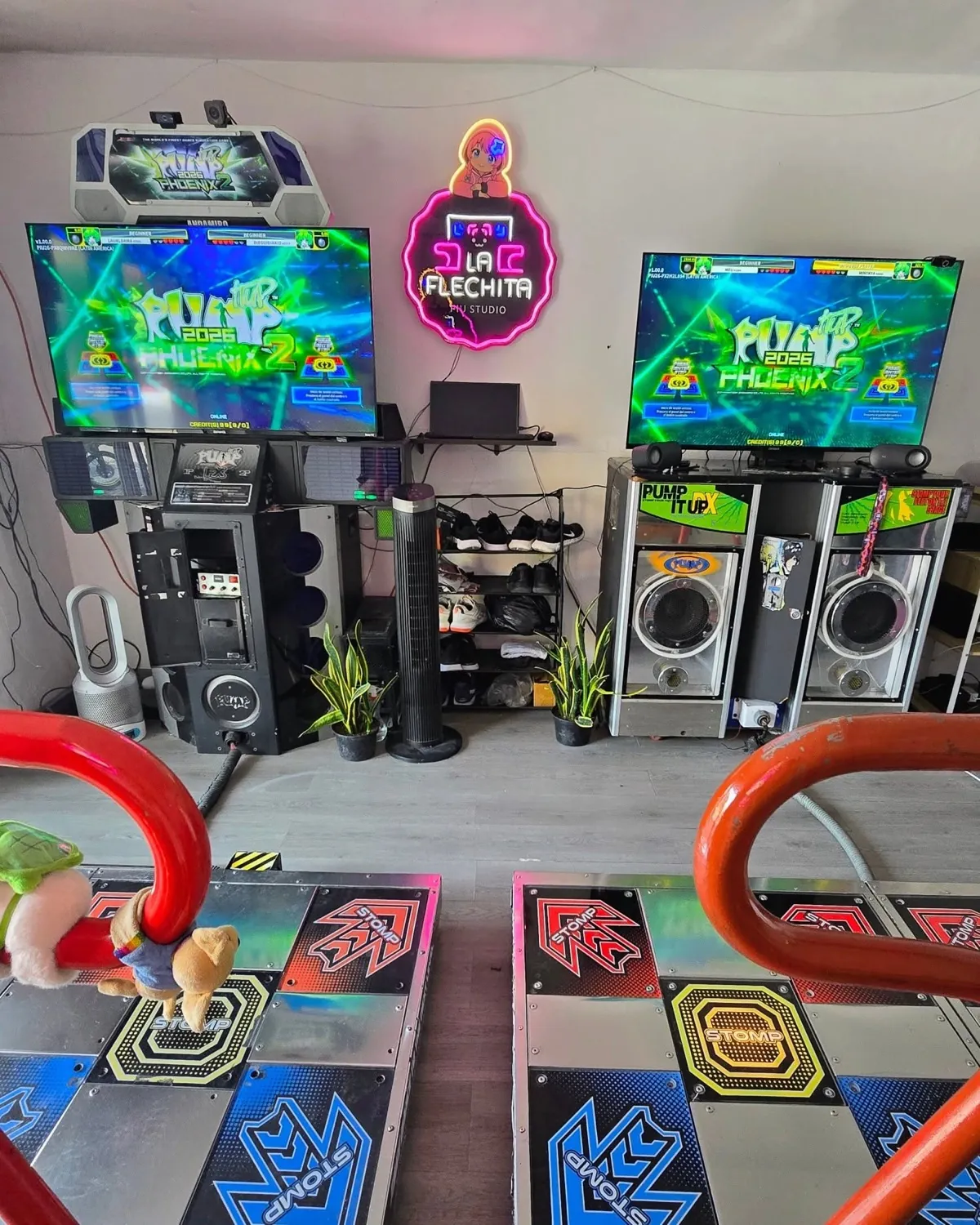 Los dos gabinetes de Pump It Up Phoenix 2 de La Flechita — FX y DX con panel TX — bajo el letrero neón del studio, arcade en Copilco, Coyoacán, CDMX